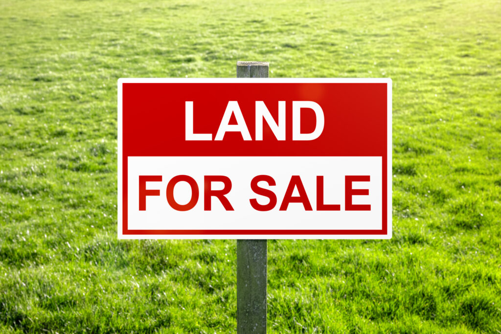 Land for sale sign in green grass field for housing development and construction - Goodfire Realty LLC